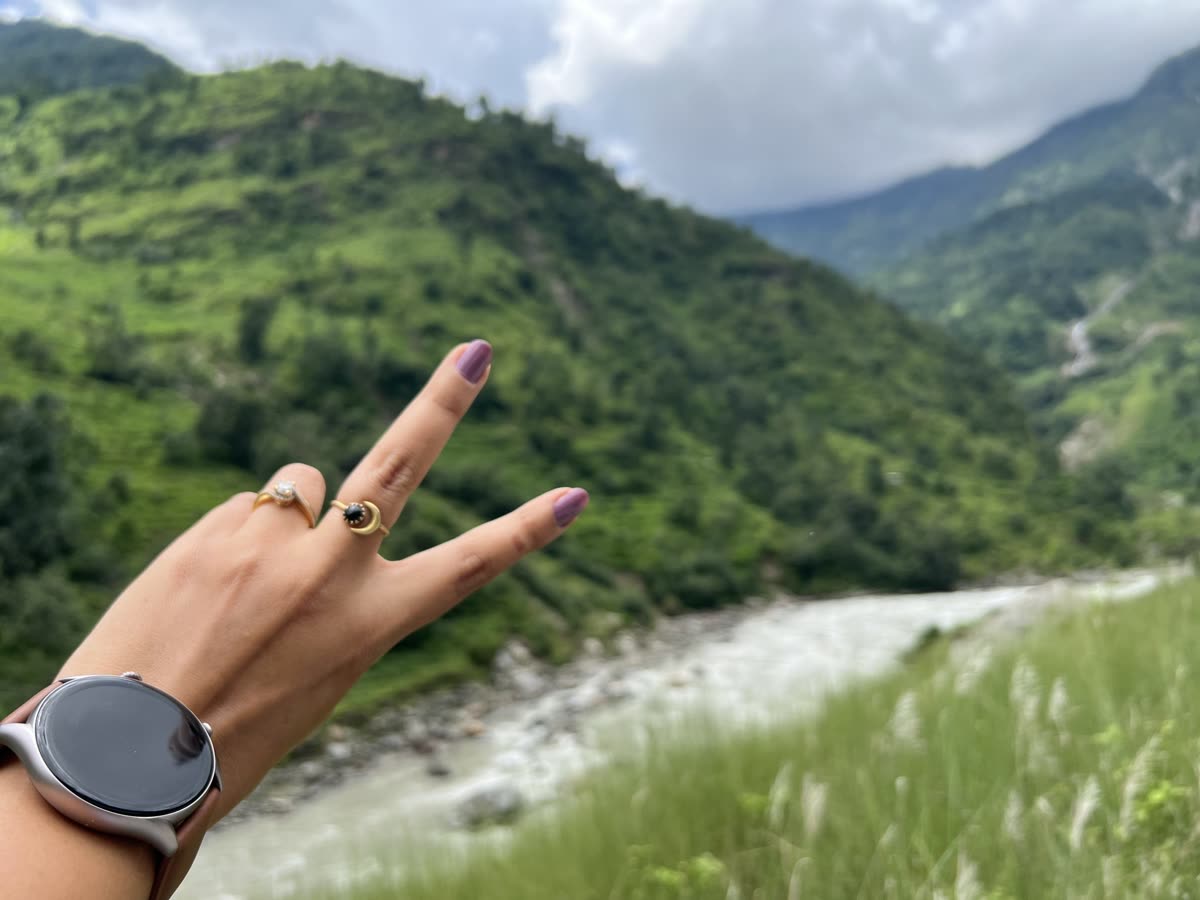 A hand with a smartwatch and two rings makes a peace sign in front of a river and green mountains — 갤럭시 워치3 초기화방법 — 워치에서 직접 vs 앱에서