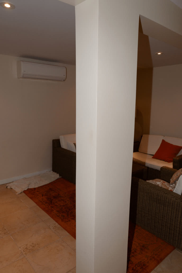 EFTA00002183 - Cozy living room with wicker furniture a red rug and an air conditioner in the corner — 지원 기기 — 에어컨·TV·조명·냉장고